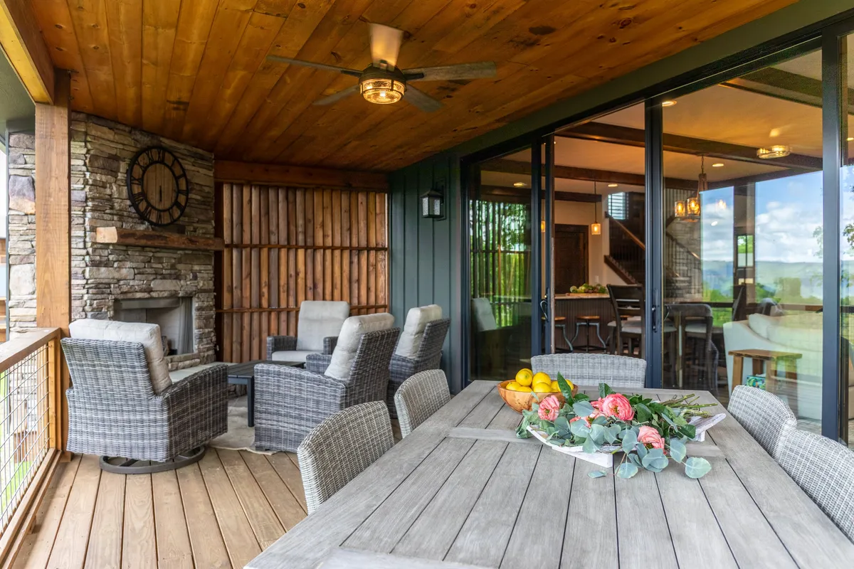 An inviting exterior seating area with a dining table set for a meal, a stone fireplace, and large glass doors opening to the outdoors. The ambiance is relaxed and welcoming, perfect for sharing meals, enjoying sunset views, or celebrating with friends and family.