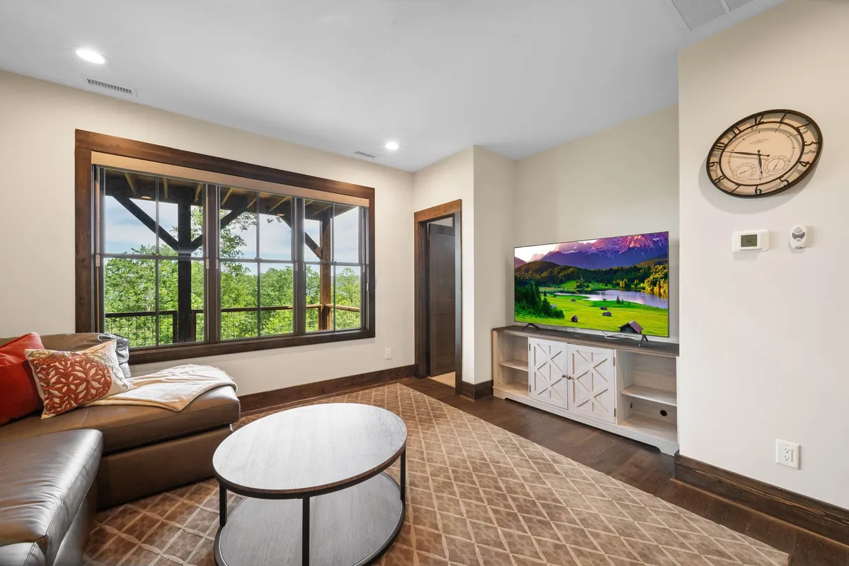 A spacious, modern living room with oversized windows offering sweeping scenic views, a comfortable sofa, and a round coffee table. The setting is ideal for relaxing, entertaining, and enjoying the surrounding landscape.