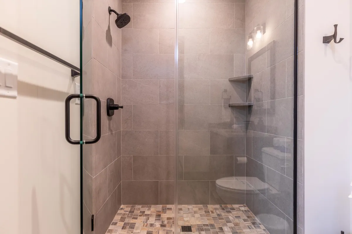 A modern ensuite bathroom with a glass shower enclosure, contemporary showerhead, and mosaic tile flooring. The space feels calm, clean, and rejuvenating—ideal for post-adventure relaxation or morning refreshment.