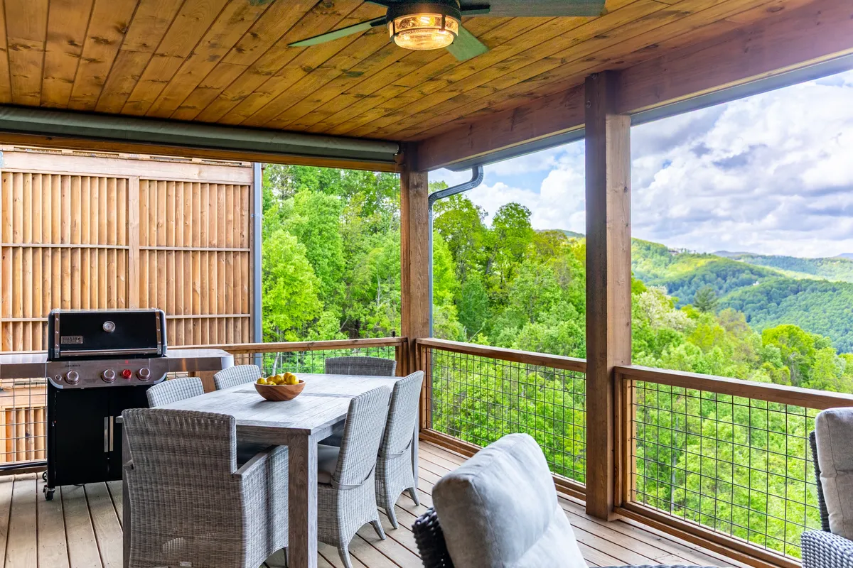 The image captures an outdoor dining area on a wooden deck, complete with a grill and table for alfresco meals. Surrounded by green landscape, it embodies the essence of outdoor feasts and gatherings in natural beauty.