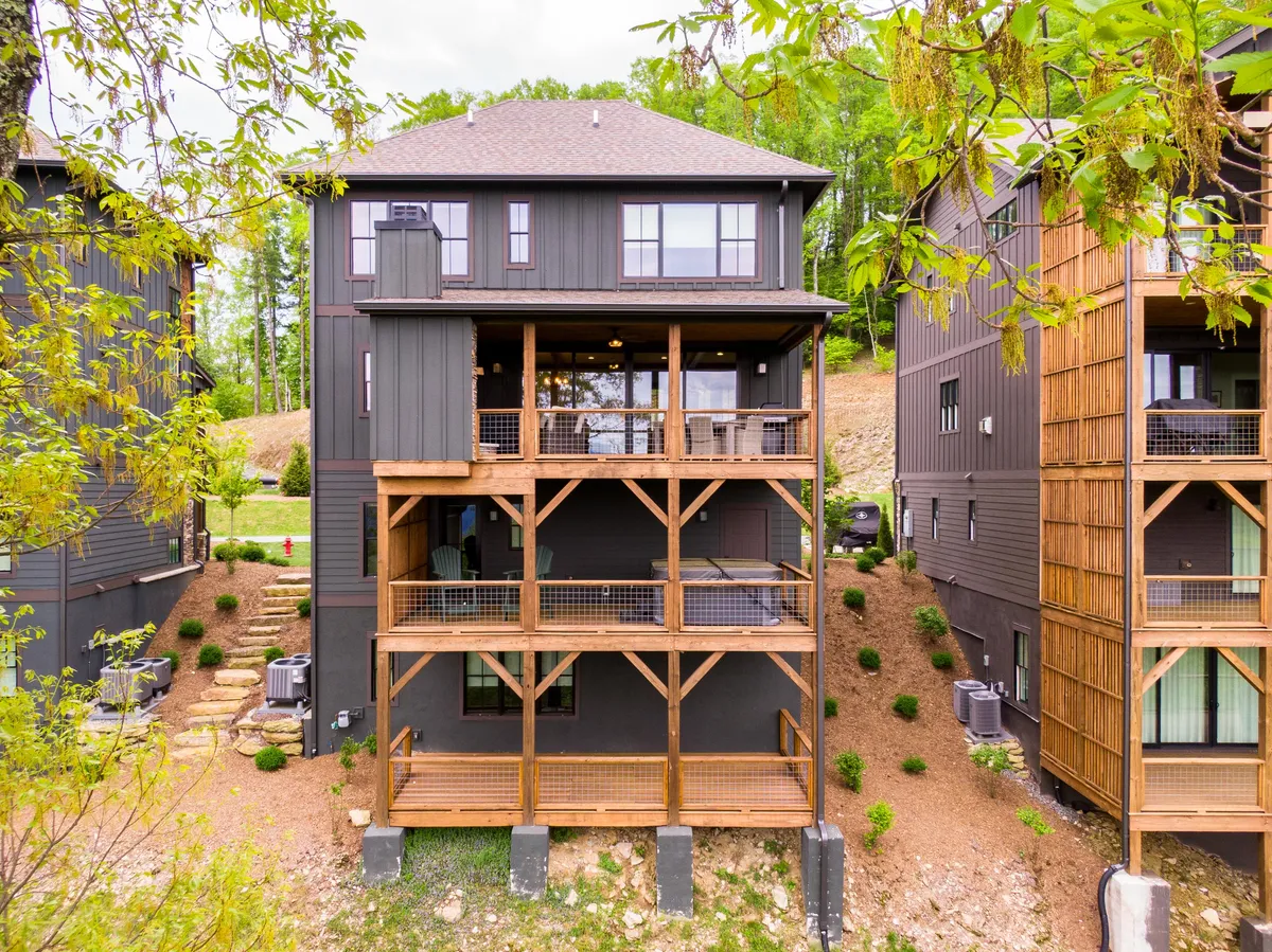 A spacious wooden deck extends from the home, bordered by lush greenery and large windows. Comfortable seating invites guests to relax or dine outdoors, and the fading light hints at beautiful sunset views and the warmth of evening gatherings.