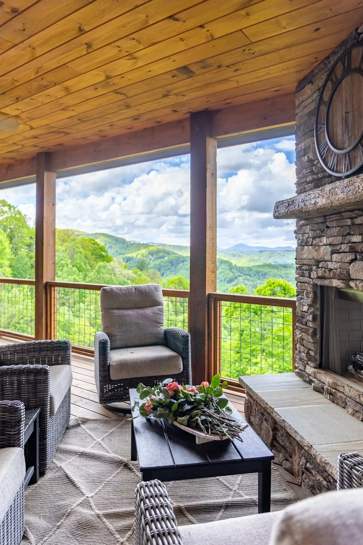 A cozy outdoor seating area with a stone fireplace overlooks sweeping mountain views. The arrangement exudes comfort and warmth, ideal for enjoying coffee at sunrise or roasting s’mores by the fire as the sun sets.