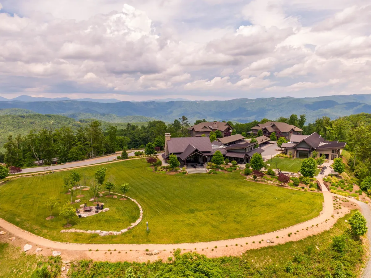 A spacious green lawn stretches out in front of multiple buildings, with a winding pathway leading toward the mountains in the background. The open area invites a variety of outdoor activities and community events.