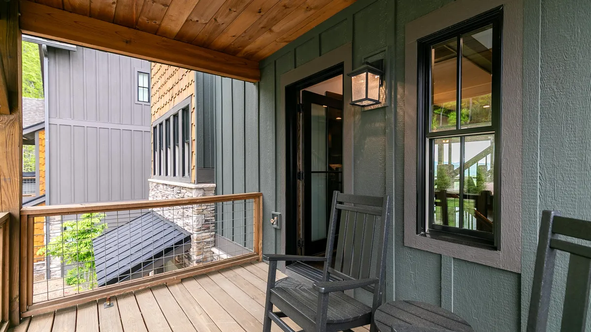 A cozy wooden deck outfitted with black rocking chairs and a lantern-style light fixture, overlooking dense greenery. The inviting porch suggests a quiet space perfect for relaxation, morning coffee, or meditative moments while immersed in nature.